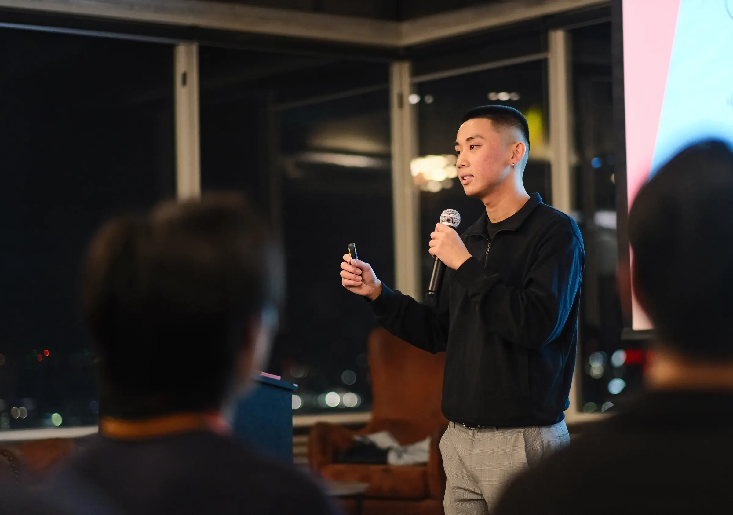 Jordan Pham speaking to a room of members at night, seen from the back of the audience